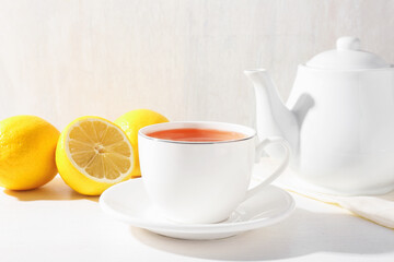 Aromatic tea in cup, lemons and teapot on white table, closeup