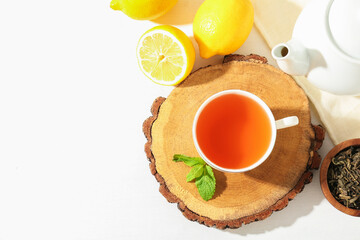 Aromatic tea in cup, lemons, mint, dry leaves and teapot on white table, flat lay. Space for text