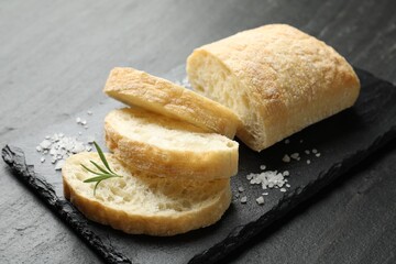 Cut crispy ciabatta, rosemary and salt on black textured table, closeup