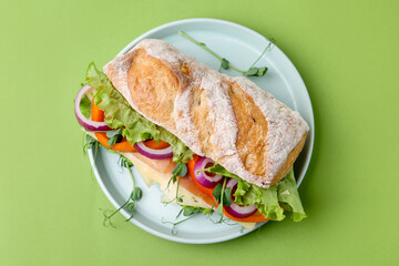 Delicious ciabatta sandwich with prosciutto, cheese and vegetables on green background, top view