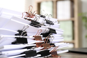 Many documents with binder clips on wooden desk, closeup