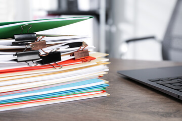 Many folders with documents and laptop on wooden desk, closeup