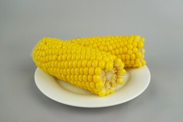 Boiled yellow corn cobs on a white plate isolated on gray background, fresh organic sweet maize close-up for healthy vegan diet and natural food design