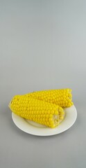 Two yellow corn cobs on white plate with gray background, boiled sweet maize vegetable close-up for organic healthy food, minimalist vegan diet concept