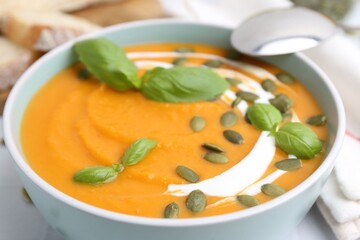 Delicious pumpkin soup with seeds and basil in bowl on table, closeup