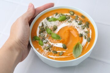 Woman with bowl of delicious pumpkin soup at light table, closeup