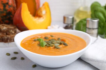Delicious pumpkin soup with seeds and basil in bowl on light table, closeup