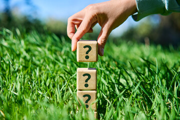 Hand placing wooden cube with question mark symbol on pyramid stack