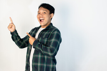 young Asian man in a green shirt smiles broadly while pointing upwards with two fingers, standing confidently against a white background.