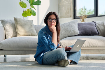 Fototapeta premium Portrait of young serious woman with laptop sitting at home
