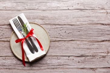 Fork, knife and a napkin tied with a red ribbon and rosemary leaves on a plate on wooden background with copy space.