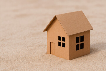 A cardboard house stands on the desert sand. Space for text.