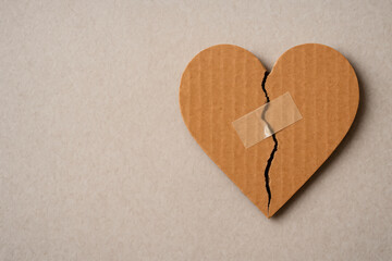 A cardboard heart with a crack sealed with tape. Space for text.