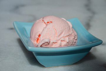 a single scoop of soft pink ice cream nestled in a pastel blue square bowl