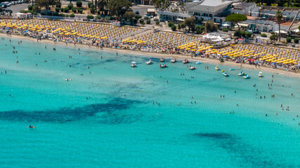 Aerial view of beach resorts and beach clubs with umbrellas and people vacationing on Mondello Beach, located near Palermo, Sicily, Italy. The turquoise water of the Tyrrhenian Sea in the foreground.