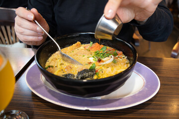 A woman eats ramen, Japanese miso ramen noodles with fried pork and egg, drizzled with sauce.