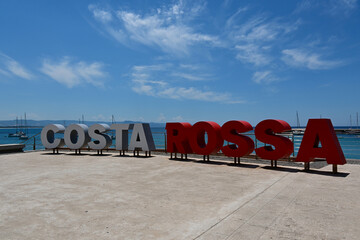 The large COSTA ROSSA lettering on the coast of Isola Rossa. A recognizable landmark of the town, often photographed by tourists. Isola Rossa, Sardegna, Italy