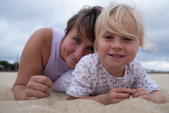Woman in sportswear relaxing on the beach with her daughter on the sand. 
