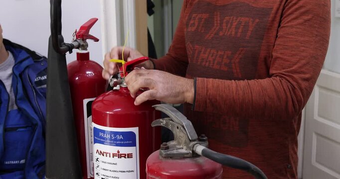 An instructional video demonstrating the correct use of a fire extinguisher, featuring clear, focused shots of hands performing the PASS technique (Pull, Aim, Squeeze, Sweep). 