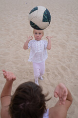 Mother teaching her 4-year-old daughter to play volleyball on the beach 