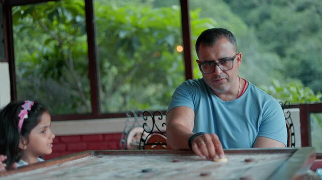 Parent and child spending leisure time together while playing carrom board game.