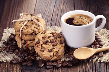 Coffee cup, chocolate chip cookies, and beans on old wooden table