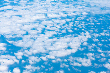 Blue sky is filled with numerous fluffy, white clouds. View from high above from an aircraft. Scattered cumulus clouds against sky

