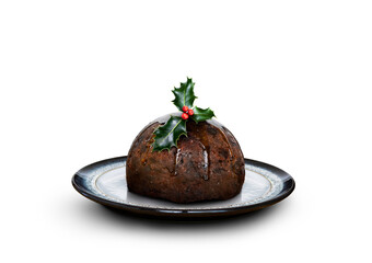 A low angle of a round patterned plate with a traditional Christmas pudding and sprig of holly on top isolated against a transparent background.
