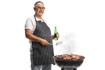 Man holding a turner utensil and a bottle of beer and grilling meat on a barbecue