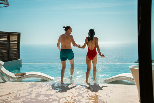 A joyful couple jumping into a swimming pool during their summer holiday.