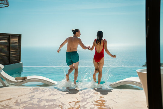 A joyful couple jumping into a swimming pool during their summer holiday.