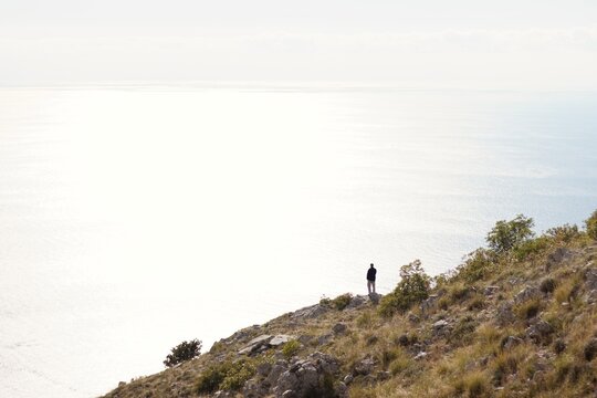 a lonely figure on the mountainside looking at the nothingness behind the mountain