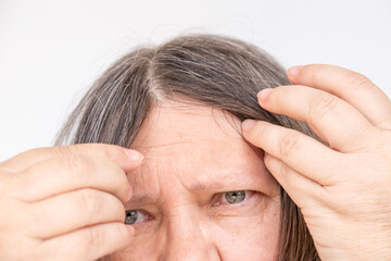 Fototapeta premium Mature woman touching her gray hair, examines silver strands, deep in thought, aging process, menopause time, emotional reflection, quiet acceptance