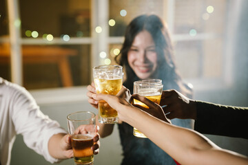 Group of friends raising glasses of beer together in a cheerful toast, celebrating with bright bokeh lights in the background.