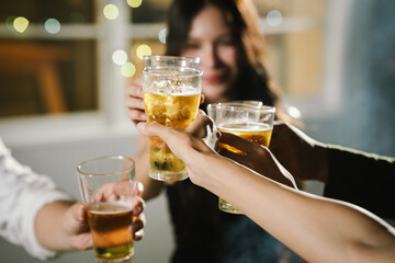 Group of friends raising glasses of beer together in a cheerful toast, celebrating with bright bokeh lights in the background.