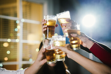 Group of friends raising glasses of beer together in a cheerful toast, celebrating with bright bokeh lights in the background.