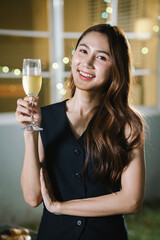 A woman smiling and toasting with a glass of wine during an evening celebration, surrounded by soft bokeh lights and a warm atmosphere.