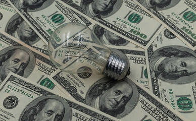 A light bulb against a background of hundred-dollar bills. A concept for saving on electricity. 