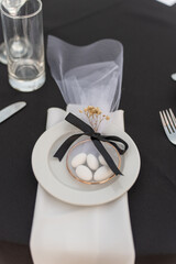 A beautifully arranged table setting showcases a decorative plate holding sugared almonds, accented with dried flowers and a black ribbon. The setting is perfect for a formal gathering.