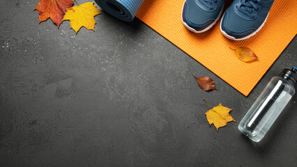 Yoga mat, fitness shoes, water bottle, and autumn leaves on a dark background for healthy lifestyle, fall fitness, and exercise concept.