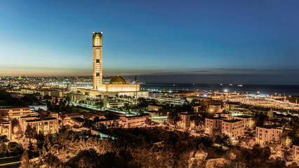 The great mosque of Algeria and the Martyr's Memorial at sunset. Buildings, and palm trees, the Marina mall parking and the coastal city bay Mediterranean sea ships enlightened under a colorful sky.