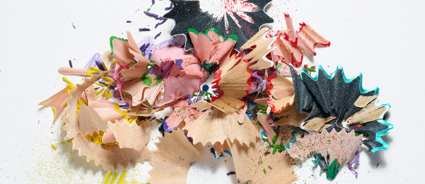 Multicolored pencil shavings and small sawdust lying in a haphazard heap on a white background.