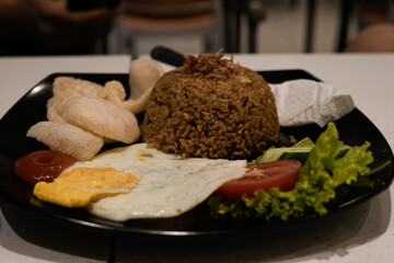  hearty Indonesian fried rice dish served with a sunny-side egg, crispy prawn crackers, fresh vegetables, and tomato slices on a sleek black plate
