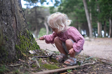 Blonde girl found a mushroom in the forest and pokes it with a stick