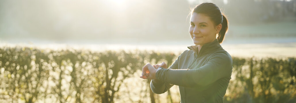 Sporty athletic young woman looks at training success on her smartwatch after exercise on a sunny winter morning	
