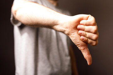 A close-up of a hand making a thumbs-down gesture, conveying disagreement, dislike, or rejection. The hand is against a neutral grey backdrop.