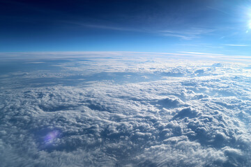 Clouds roll beneath a wingtip camera capturing blue skies and lens flare during a high altitude flight over serene landscapes