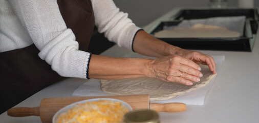 Woman hands shaping fresh pizza dough for baking in a home kitchen