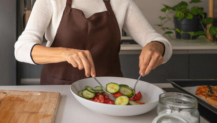 Woman in an apron preparing a vegetable salad in a kitchen, promoting a healthy lifestyle