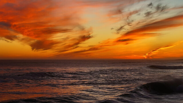 Aerial view of a fiery sunset ablaze over the ocean's dark waves, a symphony of orange and black near the coast, Cape Town, Western Cape, South Africa.